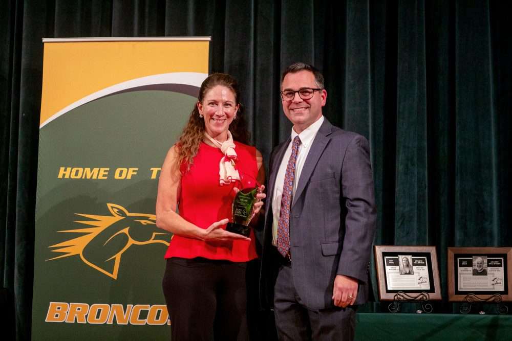 Alumna of Merit Julie Hall ’12 holding alumni award next to Provost Brower.