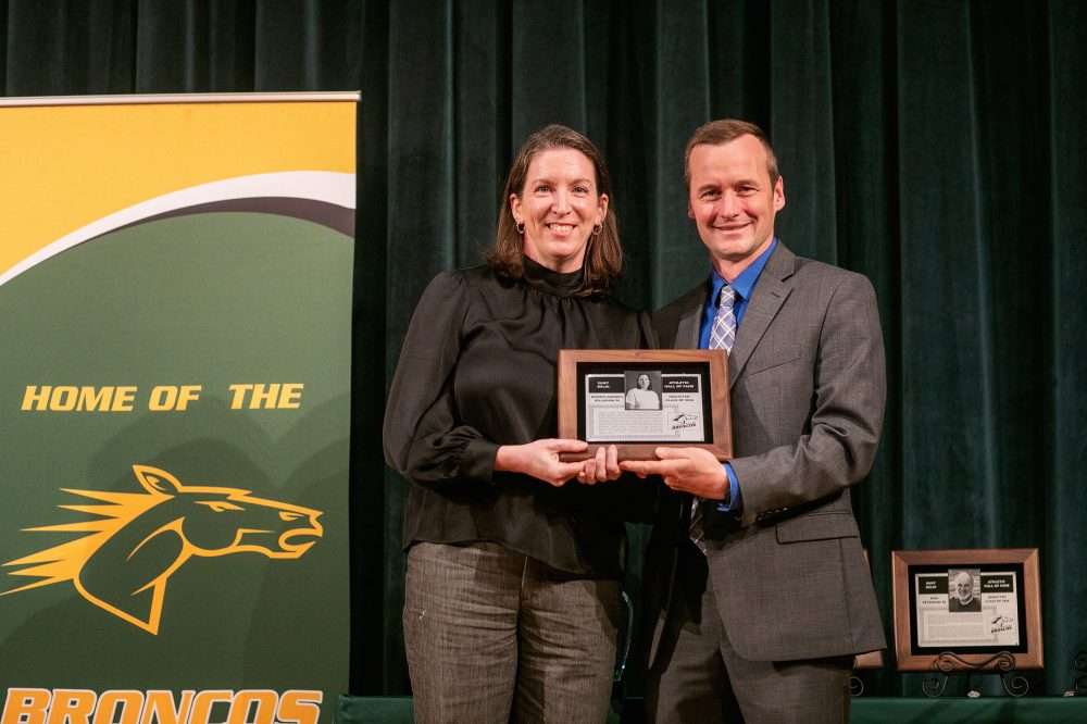 Jennifer Williamson '04 holds an alumni award plaque next to athletic director Robb Munro.