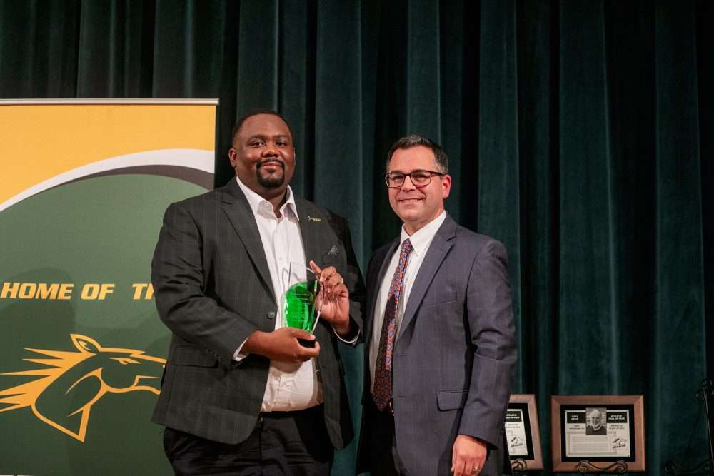 Alumnus of Merit: Antoine Noble ’13 hold an award next to Provost Brower.