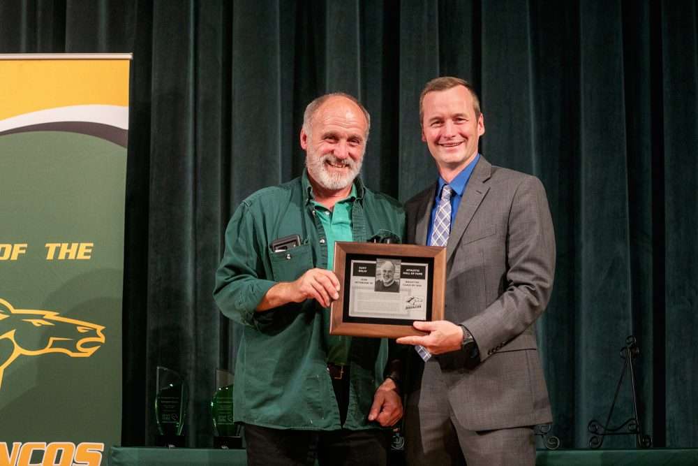 Don Peterson ’84 holds an alumni award next to athletic director Robb Munro.