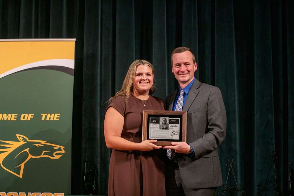 Nicole Welcome ’14 holds an Athletic Hall of Fame induction plaque at alumni awards next to athletic director Robb Munro.