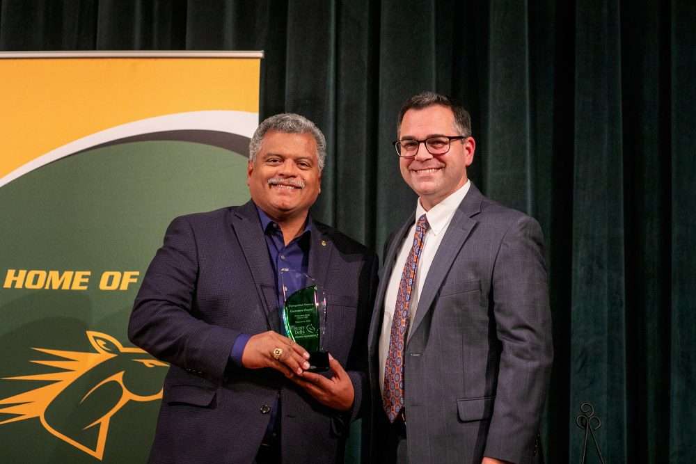 Distinguished Alumnus: Geovanny Osorio ’89 holds an alumni awards green trophy next to Provost Brower.